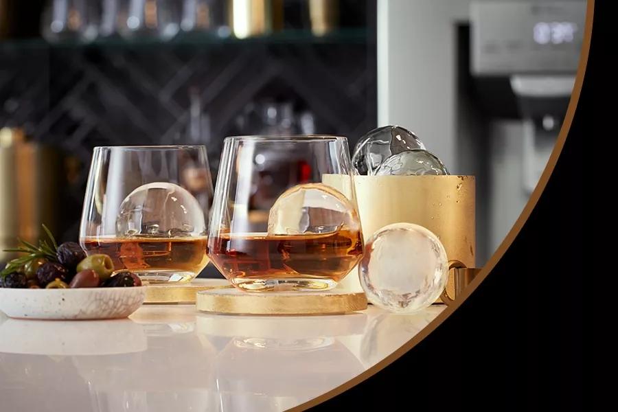 Alcoholic tumbler glasses on a table surrounded by ice and fruit