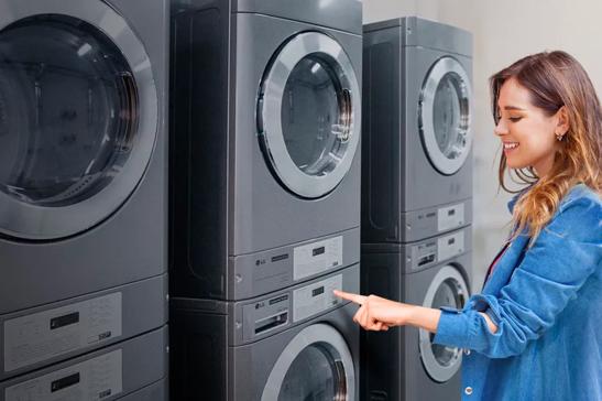 A woman interacts with a row of stacked commercial washing machines, pointing at a control panel.