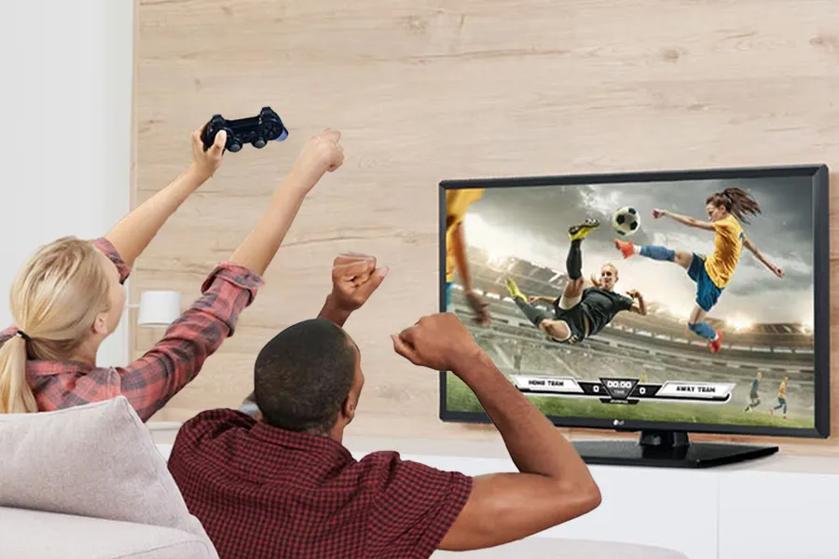 Two people playing a soccer video game on an LG TV, with one holding a game controller.