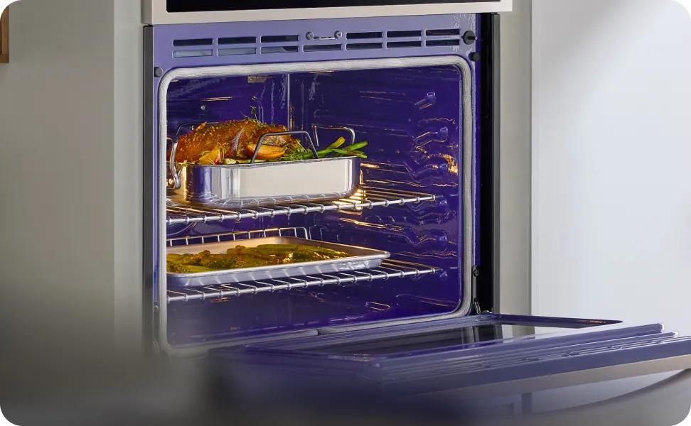 An open oven shows a turkey roasting on the top rack and a tray of vegetables roasting on the bottom rack.