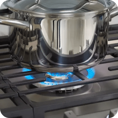 A pot sits on a cast iron grate over blue flames from a gas cooktop.