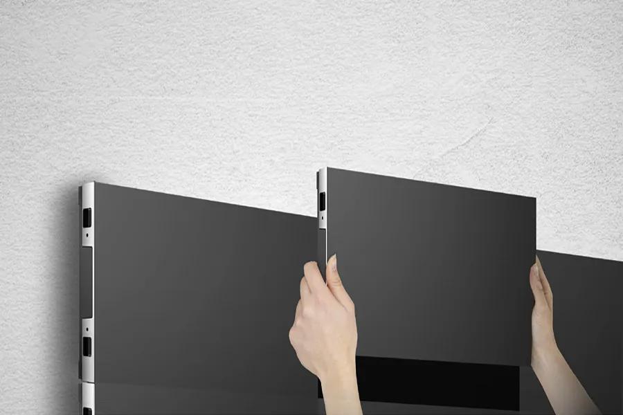 Hands installing a dark gray panel next to another similar panel on a light gray surface.