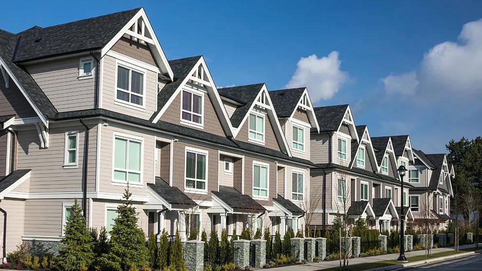 Row of modern multifamily townhomes with gray siding, gabled rooflines, and landscaped front yards under a blue sky