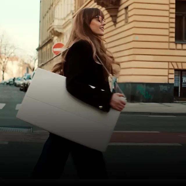 A woman carries a detached StanbyME 2 portable touchscreen with a shoulder strap across a city street. 
