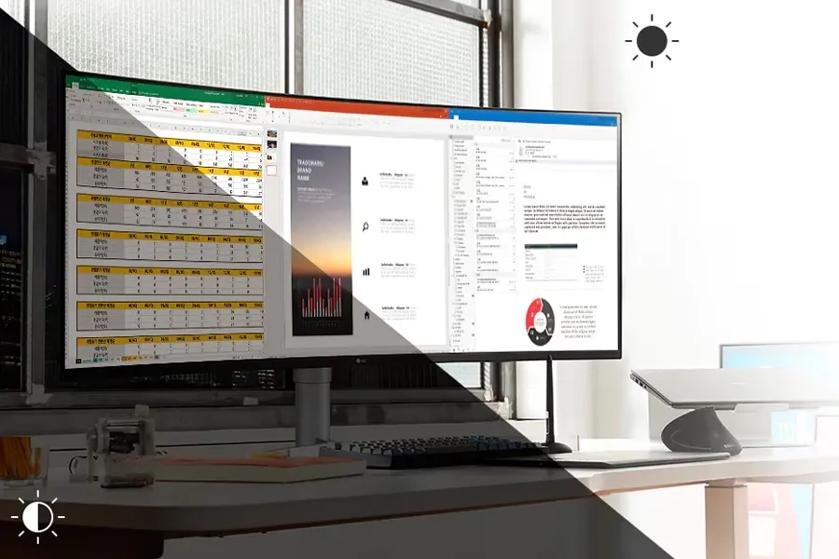 Bright office workspace with a wide monitor displaying a spreadsheet and a document.