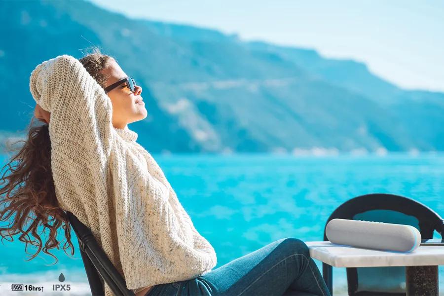 Image of a woman sitting by the water in the sun with a stanbyME speaker on the table