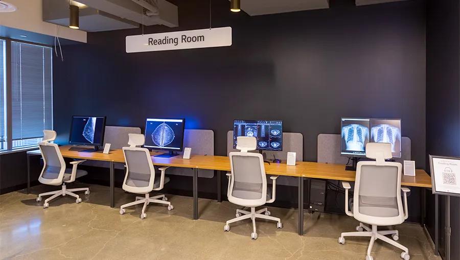 Reading room at LG LA Business Innovation Center. A long desk holds four diagnostic monitors displaying various x-ray and medical scan readouts, with desk chairs before them.