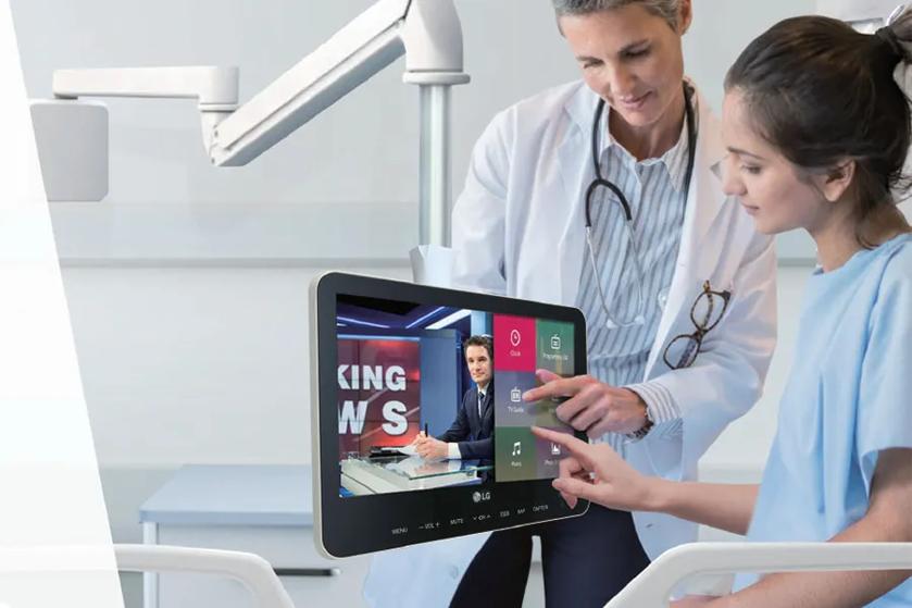A patient and a healthcare professional using a touch-screen LG TV in a hospital room.