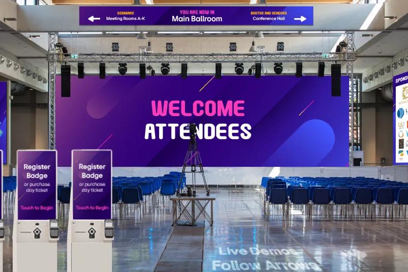 A large ballroom space set up for a conference, with Direct View LED as a stage backdrop, projectors and signage for wayfinding, and touch kiosks for tickets.