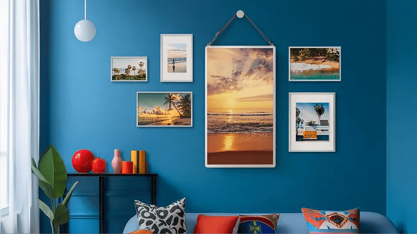 LG StanbyME 2 displayed as a digital picture frame on a blue wall, showing a sunset photo as part of a gallery wall arrangement.