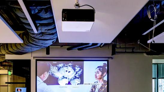 An LG ProBeam projector mounted from the ceiling of the LG LA Business Innovation Center, projecting a video onto a screen on the wall.