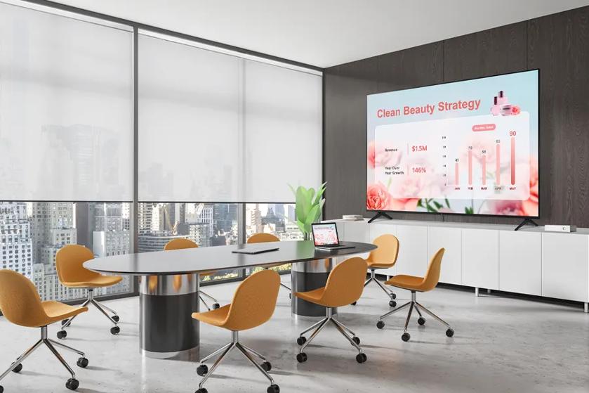 A modern conference room with orange chairs, a large table, and a presentation on a TV titled "Clean Beauty Strategy."