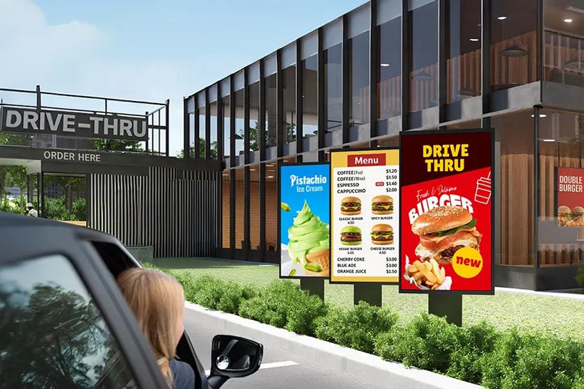 Drive-thru with illuminated menu boards and a car approaching.