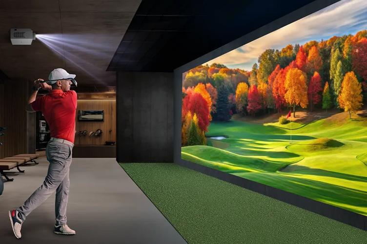  an indoor golf simulator with a golfer swinging and a vibrant autumn landscape projected on the wall.