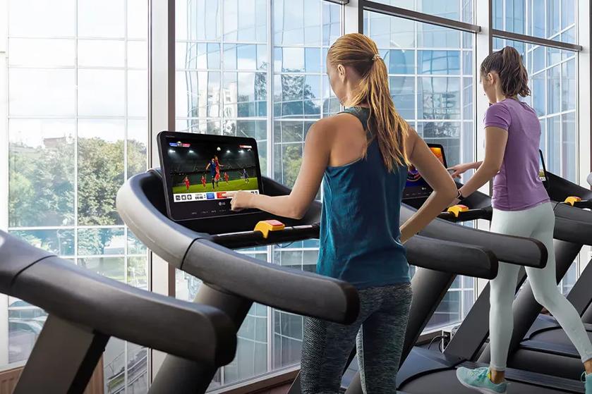 Two women exercising on treadmills, viewing LG displays with digital content.