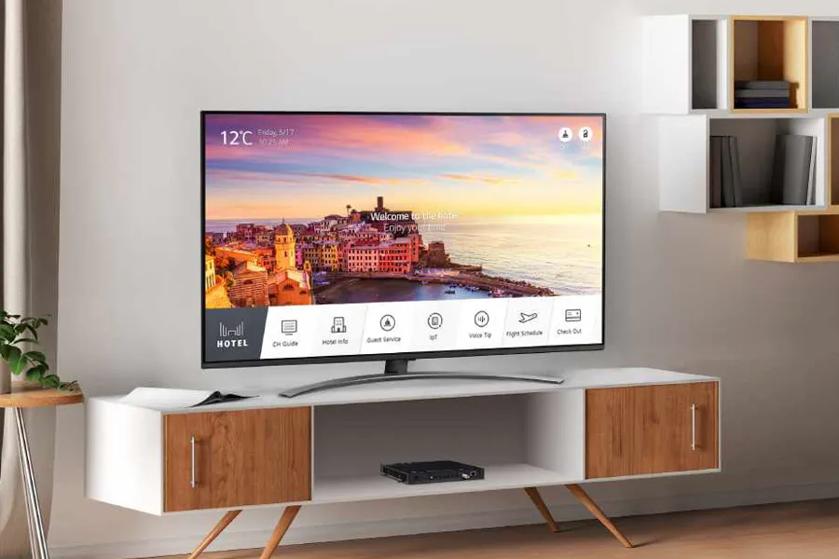 Modern living room with a flat-screen TV displaying a coastal town at sunset. TV stand with wood finishes and wall shelves.