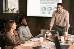 Group of professionals in a meeting, with LG laptops on the conference table and a projected business presentation behind them.