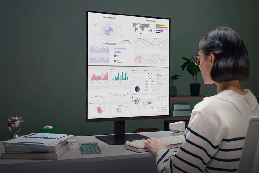 A woman at a desk using a computer monitor displaying graphs and charts.