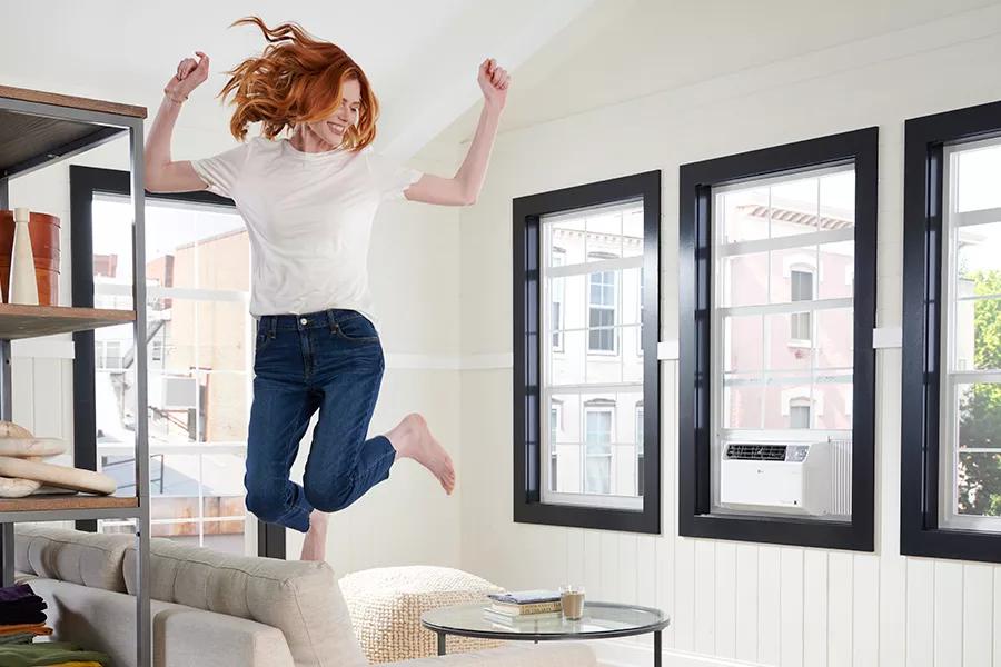 LG window air conditioner in a living room and a woman jumping on a sofa