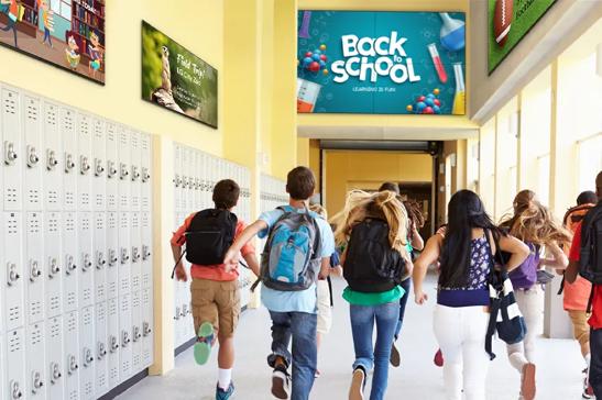 Excited schoolchildren run down the hall of a school. Various LG digital  displays line the walls, welcoming students back to school and displaying information for educational events.
