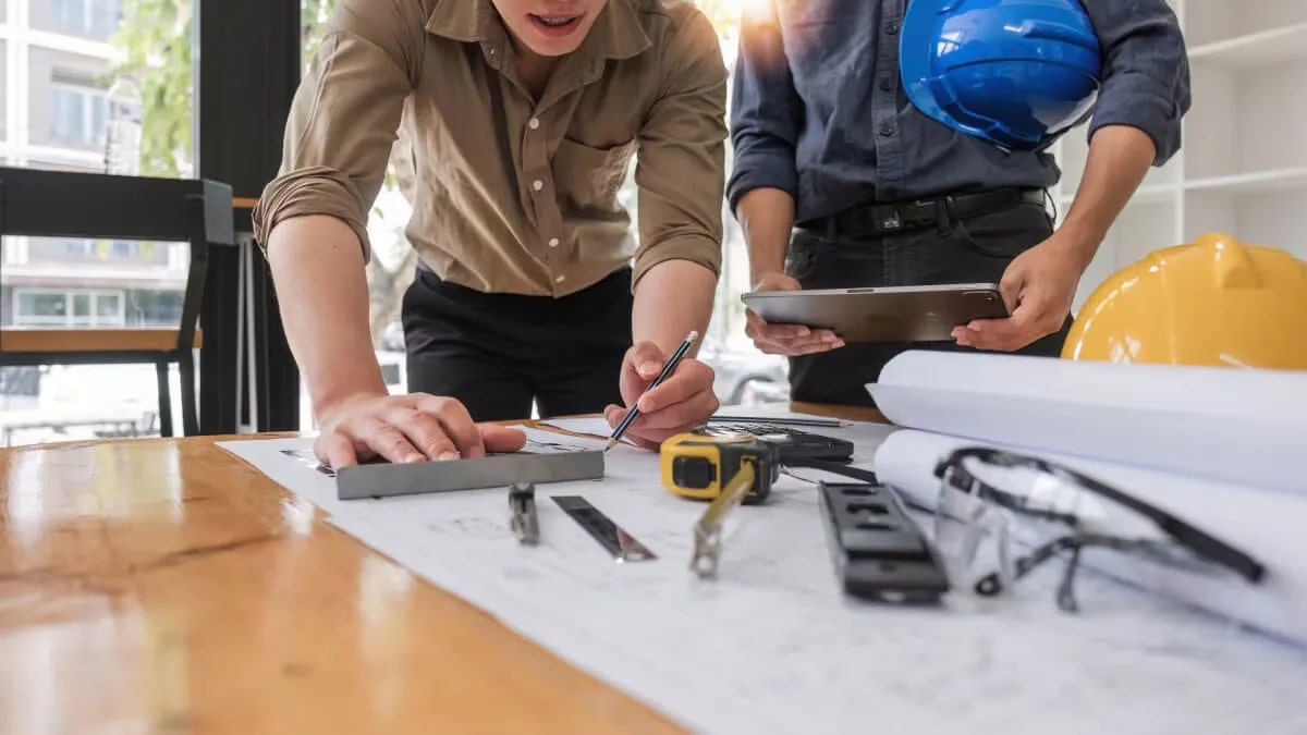 Contractors looking over building plans with various architectural instruments on the table.