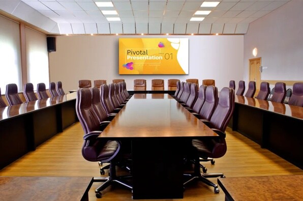 A large conference room with a long wooden table, leather chairs, and a presentation screen at the far end.