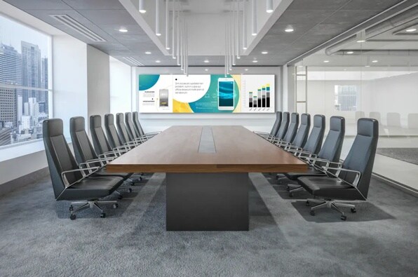 Modern conference room with a long table, surrounded by chairs, a large screen, and a window view of skyscrapers.
