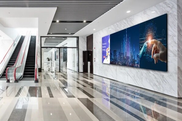 Modern building lobby with escalators and digital displays on the wall.