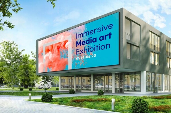 A modern building with a billboard advertising an "Immersive Media Art Exhibition" featuring abstract pink and coral designs on a blue background.
