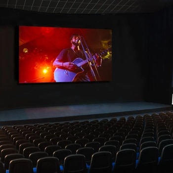 Movie theater showing a performer playing guitar and singing on screen, with rows of empty seats.1