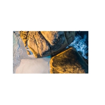 Aerial view of golden-brown coastal rocks, pale sand, and foaming blue ocean waves.1