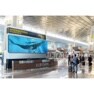 An information desk in a modern airport terminal with a large screen displaying whales underwater.