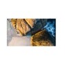 Aerial view of golden-brown coastal rocks, pale sand, and foaming blue ocean waves.