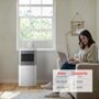 LG Portable Air Conditioner in bright home office with person working on laptop, showing area coverage chart of 150 SQ FT/5,000 BTU and 250 SQ FT/6,000 BTU