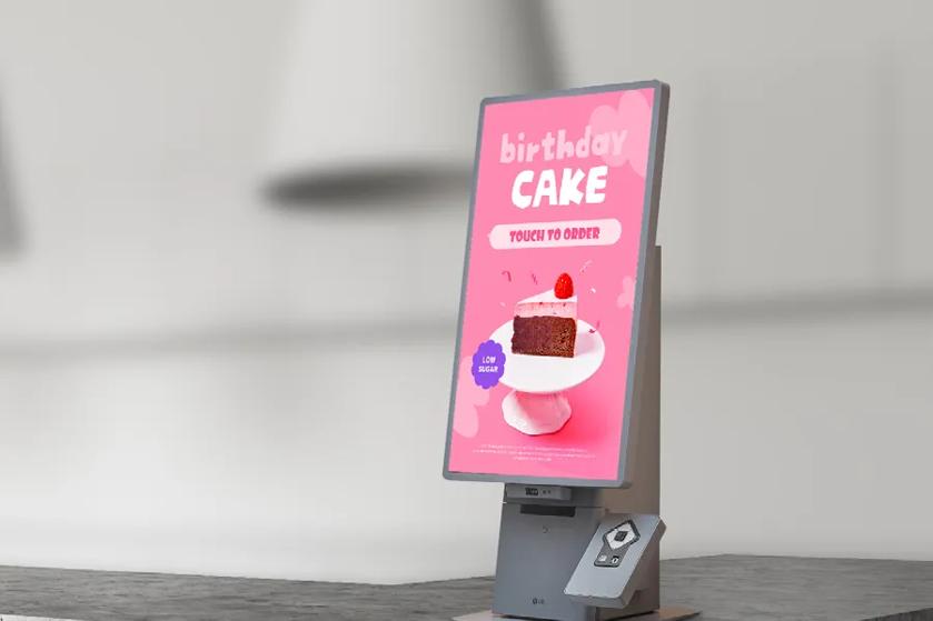 Digital kiosk displaying a birthday cake advertisement on a pink background.