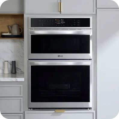 Built-in LG microwave above a wall oven in a tall cabinet, both stainless steel, centered between drawers and open shelving in a modern kitchen.