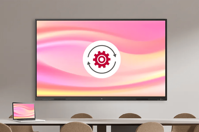 A large screen with a pink-yellow gradient and gear graphic, above a table with a laptop displaying the same image.