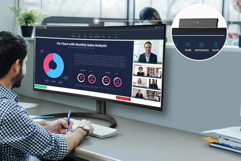 A man is participating in a video conference, with a pie chart and participant videos displayed on his widescreen monitor.