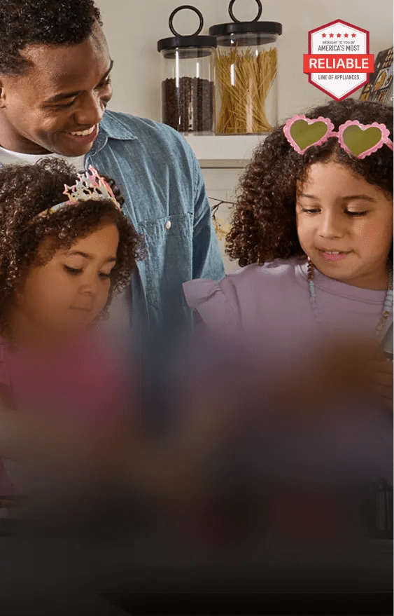 Two young girls play dress-up in a kitchen with an LG refrigerator as they prepare a healthy snack with their dad.