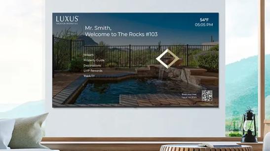 Digital screen displaying a pool and landscape with text "Mr. Smith, Welcome to The Rocks #103."