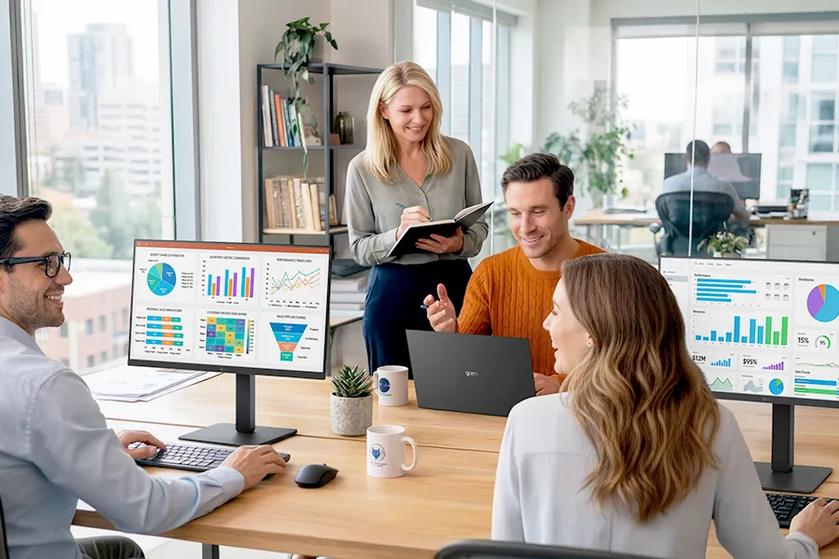 Four coworkers laugh and smile as they work using LG monitors at an open concept desk