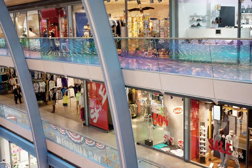 Transparent signage featuring decorative patterns and advertisements on a shopping mall upper level railing. 