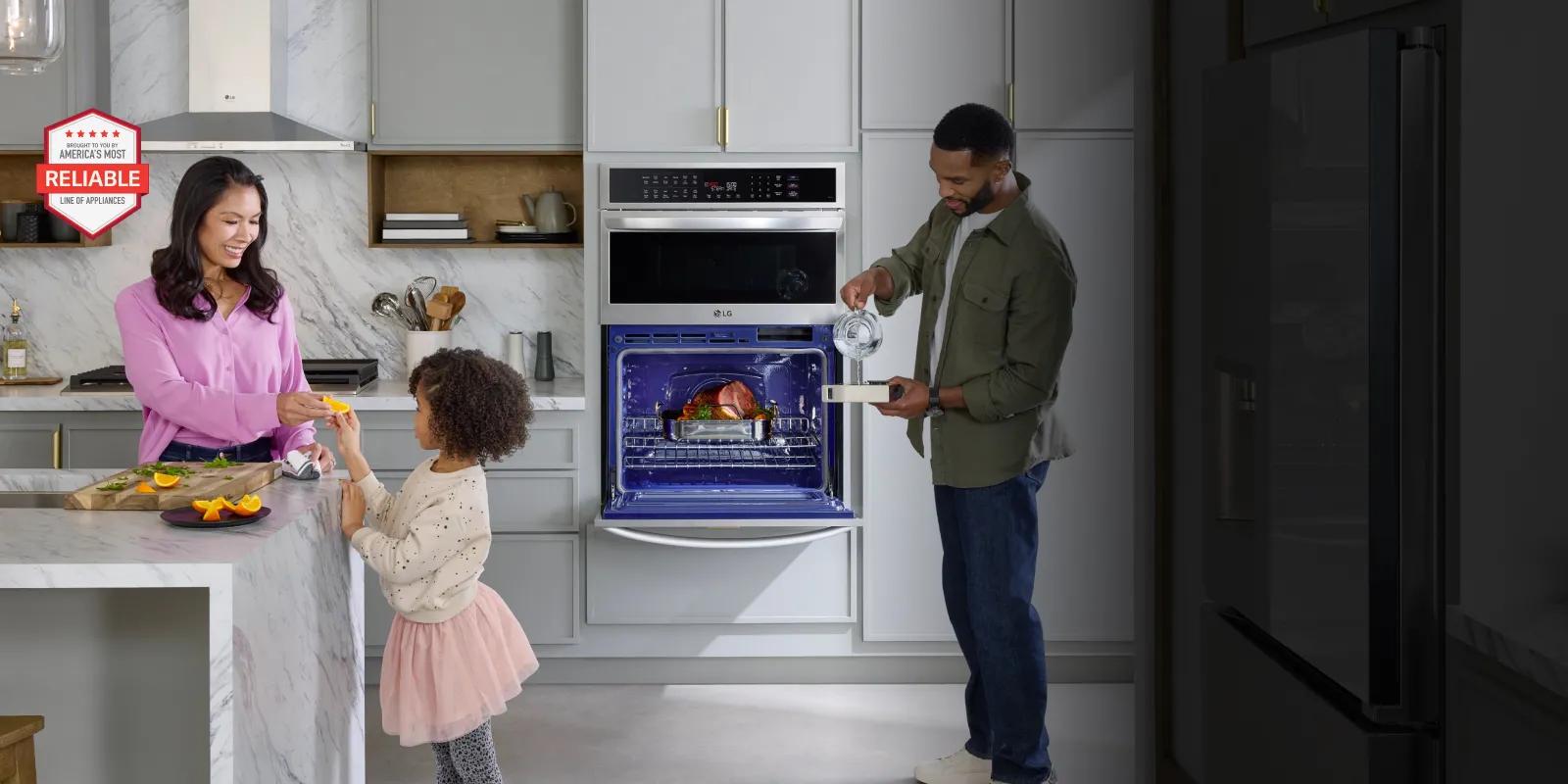 A mother slicing oranges for her daughter at the kitchen island while the father cooks a ham in their LG wall oven.