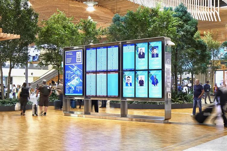 Interior of the Portland Airport, with LG wayfinding digital signage displaying flight information, airport map, and other info. The signage is surrounded by the wood details and green foliage of the airport.