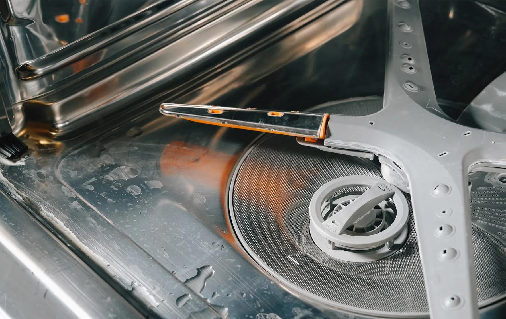The interior floor of an LG dishwasher is covered in food debris and hard water stains. - Before