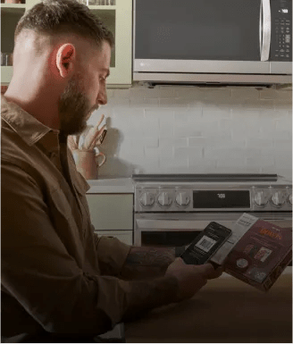 A man sitting in the kitchen using the ThinQ app on is phone to scan the bar code of a frozen meal - mobile.