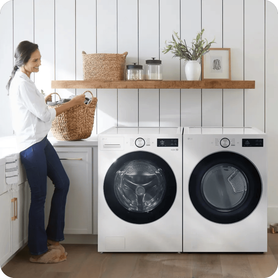 A woman holds a basket of linens next to an LG washer and dryer pair in a brightly lit laundry room with white accents.