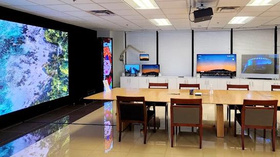 Interior of the LG Business Innovation Center in Atlanta, with a conference table next to a row of LG computer monitors. The left wall is taken up with a large projector screen displaying graphics from an LG ProBeam projector mounted above the conference table.